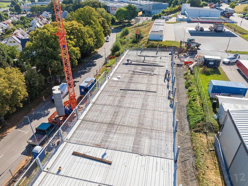 Crane over a construction site with workers and surrounding streetscape and landscape, car park construction, Calw, Germany