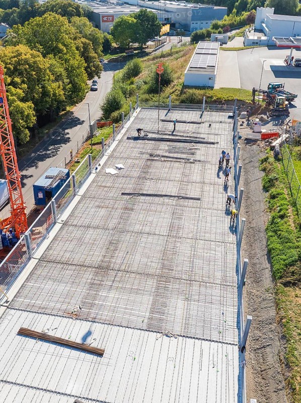 Workers on construction site with crane in sunny weather, surrounded by roads and fences, car park construction, Calw, Germany