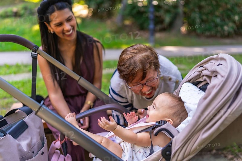 Grandmother and mother taking care of a baby girl in a stroller, playing and laughing together in a park