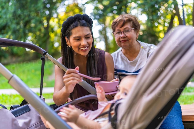 Mother feeding her baby girl with grandmother watching, enjoying family time together at the park