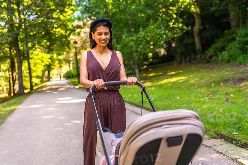 Latin mother enjoying a walk in the park, pushing a stroller with her baby inside, on a sunny day