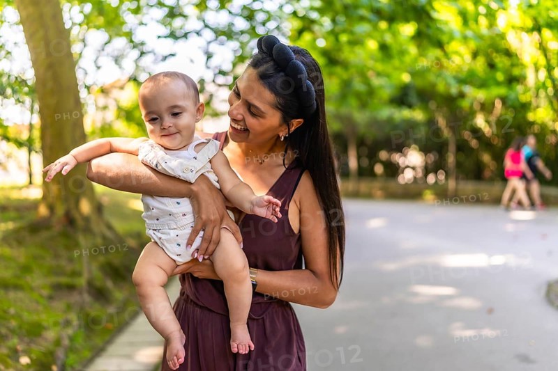 Happy latin mother holding and playing with her baby daughter in a park, enjoying a sunny day outdoors