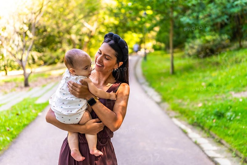 Latin mother holding her baby daughter, smiling and enjoying a walk in a park during a sunny day