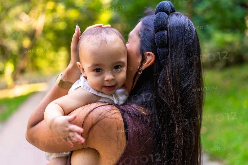 Mother cuddling her baby girl while strolling through a park, savoring a sunny day filled with family love and joyful bonding