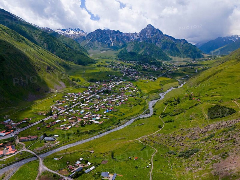 Wide valley with river and village, surrounded by mountains under a partly cloudy sky, aerial view, view into the valley of the river Terek, Toti, Kazbegi, Qasbegi, Stepantsminda, Georgian Military Road, Mtskheta-Mtianeti Province, High Caucasus, Georgia