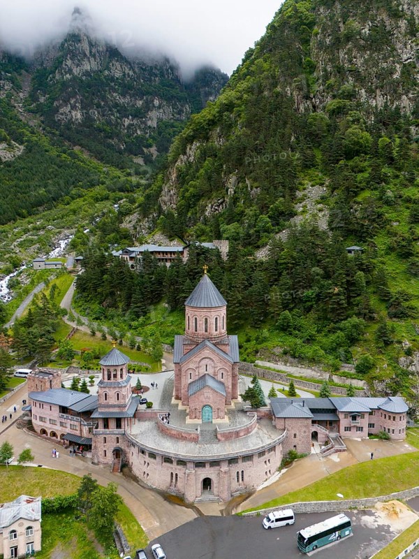 Majestic red brick church in a picturesque mountain landscape under cloudy atmosphere, aerial view, Dariali monastery complex, located in the Dariali gorge of the Tergi river, Terek, Khevi mountain region, Georgian Military Road, Mtskheta-Mtianeti province, High Caucasus, Georgia