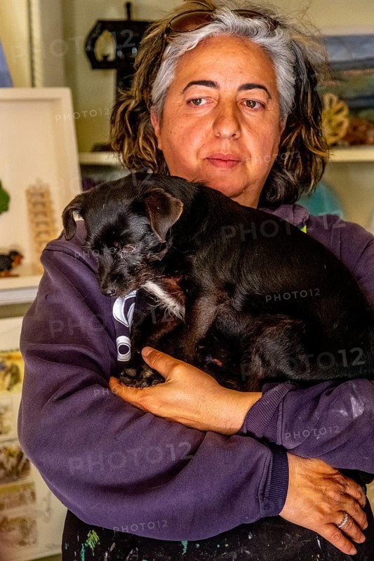Sardinia, Pina Monne, portrait of woman and dog on arm, artist, Tinnura, Europe, Oristano province, Italy, arm, expression, gaze, detail, woman, middle-aged woman, portrait of woman, face, pet, dog, interior, interaction, small town, context, culture, artwork, painting, human, facial expression, portrait, pose, region, sight, sightseeing, style, animal, animal husbandry, animal love, tourism, tradition, environment, European, artistic, local, Mediterranean, female