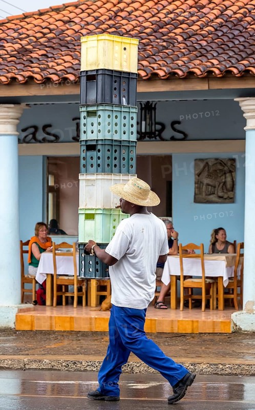 Cuban man with hat carrying and balancing crates of drinks across a street in Vinales, Viñales, Cuba, Pinar del Río, Viñales, Pinar del Río