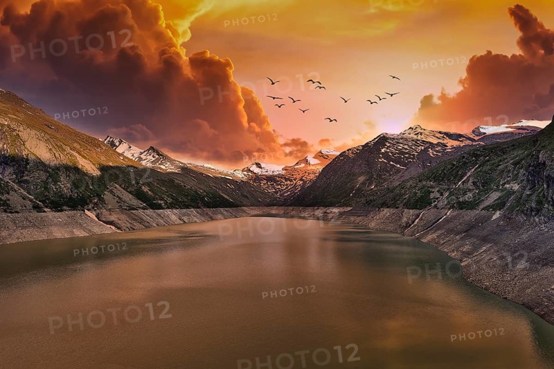 Dramatic sunset over a mountain lake with flying birds and clouds, Mattmark Reservoir, Saas Almagell, Saas Grund, Canton Valais, Switzerland