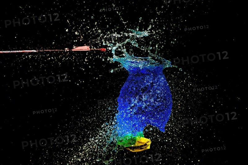 A blue water balloon bursts bubbling, with an arrow and yellow elements in a haunting scene, high speed shot, water balloon, arrow