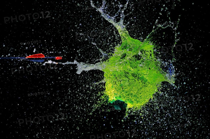 A green water balloon bursts powerfully under the impact of an arrow, against a dark background, high-speed shot, water balloon, arrow