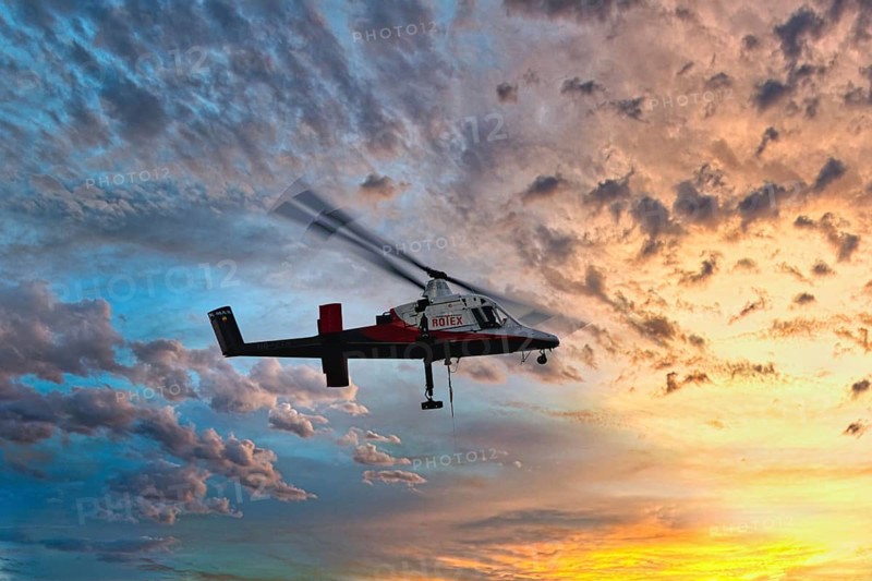A helicopter flies in front of a colourful sunset with dramatic cloud formations, transport helicopter, timber transport, Saas Grund, Canton Valais, Switzerland