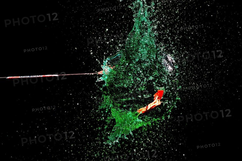 A green water balloon explodes under the impact of an arrow against a dark background, high-speed shot, water balloon, arrow