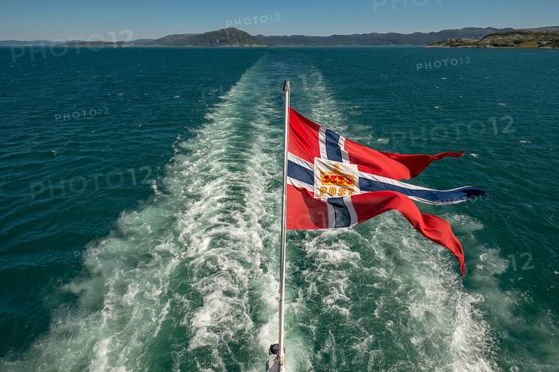 The post symbol on Norwegian flag of a Hurtigruten ship, foaming spray, Trondheimfjord, Agdenes, Trøndelag, Norway, Scandinavia, Europe, adventure trip, fjord, flags, tourism, Hurtigruten, Hurtigruten trip, cruise, NOR, mail ship, travel, destination, sea trip, sightseeing, tourism, Trøndelag, Norwegian, Scandinavian, touristic