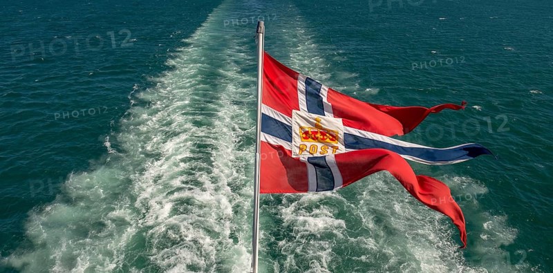 The post symbol on Norwegian flag of a Hurtigruten ship, foaming spray, Trondheimfjord, Agdenes, Trøndelag, Norway, Scandinavia, Europe, adventure trip, fjord, flags, tourism, Hurtigruten, Hurtigruten trip, cruise, NOR, mail ship, travel, destination, sea trip, sightseeing, tourism, Trøndelag, Norwegian, Scandinavian, touristic