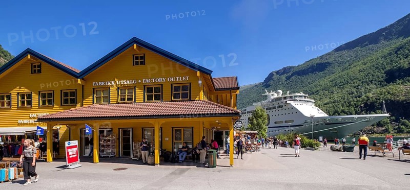 Tourists in Flåm, FABRIK KUTSALG FACTORY OUTLET, shops, yellow wooden house, excursion boat, fjord, mountain, trees, blue sky, Sogn og Fjordane, Norway, Scandinavia, Europe, Flåm, NOR, travel, tourism, destination, sightseeing, sea voyage, Hurtigruten, Hurtigruten trip, tourism, Norwegian, Scandinavian, tourist, cruise, adventure trip, pedestrian, river, forests, shipping, shops, shopping, shopping, signs, flags