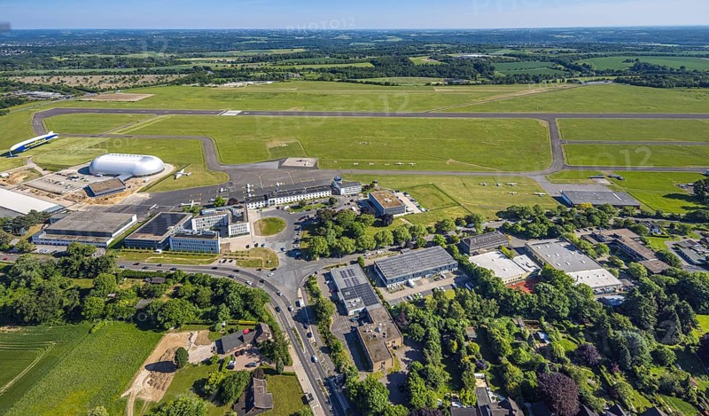 Aerial view, Essen/Mülheim Airport, Goodyear airship Zeppelin, construction site next to the WDL airship hangar, construction site and new office buildings with multi-storey car park (Pitstop centre), parked aircraft, runway and landing strip, Holthausen - Southeast, Mülheim an der Ruhr, Ruhr area, North Rhine-Westphalia, Germany, construction work, construction area, building site, building plots, construction project, construction site, DE, Europe, aerial view, aerial photography, aerial photography, overview, bird's-eye view, overview