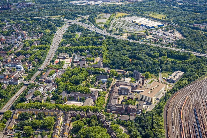 Aerial view, Hamborn municipal park, on the right Helios St. Johannes Klinikum Duisburg at the marshalling yard and abbey cemetery with St. Johann, abbey grammar school and abbey primary school, Gottfried-Wilhelm-Leibniz comprehensive school public school, above motorway junction Duisburg-Nord and Ikea furniture store, Alt-Hamborn, Duisburg, Ruhr area, North Rhine-Westphalia, Germany, railway area, burial ground, education, educational institution, DE, Europe, cemetery, memorial site, comprehensive school, railway tracks, tracks, Gottesacker, large construction site, primary school, graves, burial ground, grammar school, educational institute, aerial view, aerial photography, aerial photography, resting place, school, overview, bird's-eye view, forest, birds-eyes view, overview