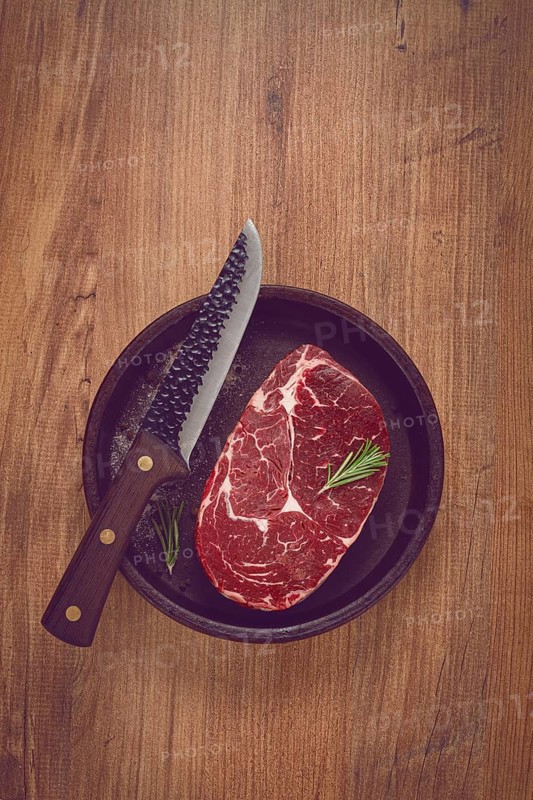 Steak made from fresh beef, with herbs and various spices, in a clay pan, with a kitchen knife, ready to cook, no people