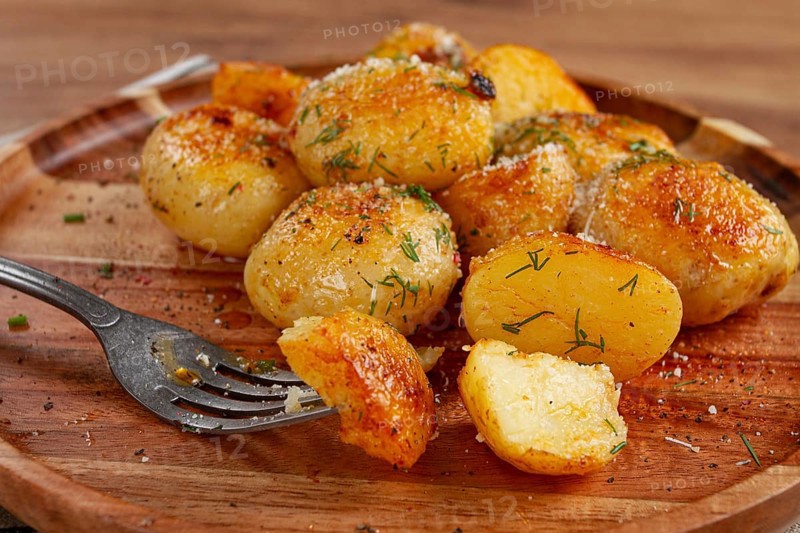 Half-eaten fried new potatoes, with butter and dill, on a wooden plate, with a fork, at home, without strangers