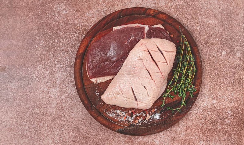 Fresh raw duck breasts, on a wooden chopping board, with herbs and spices, no people