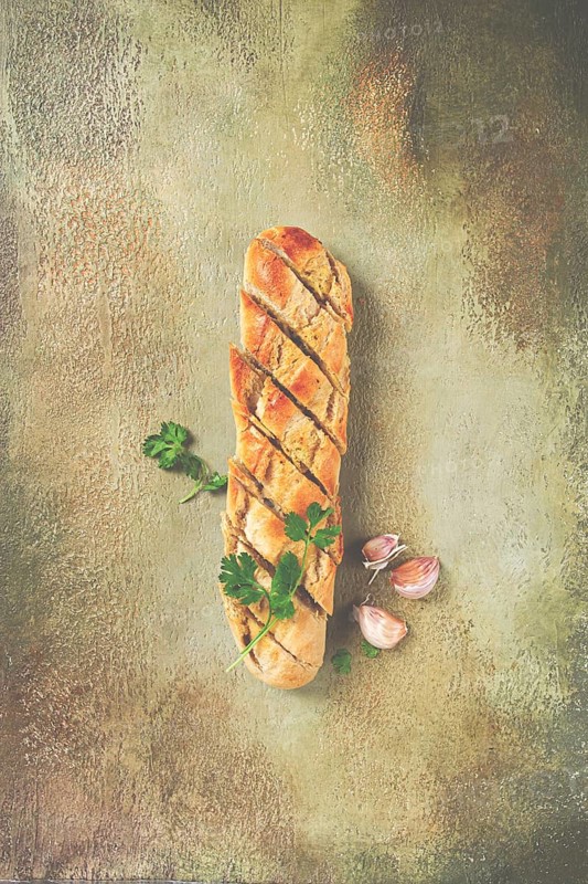 Garlic bread, baguette with garlic butter and herbs, with herbs and garlic cloves