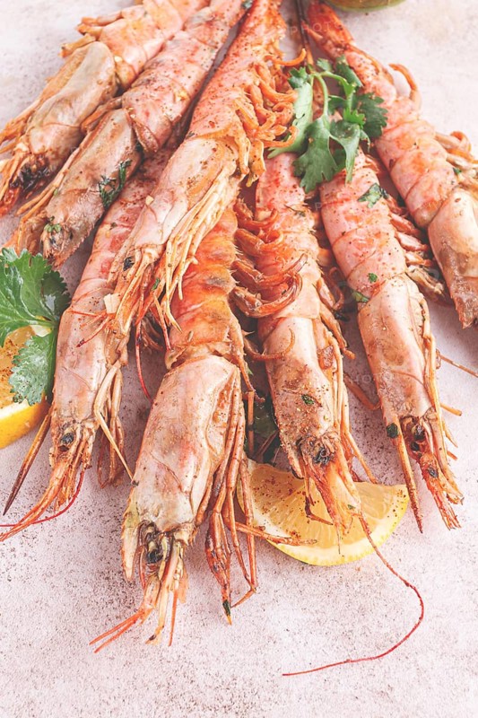 Shrimps on skewers, Grilled, spread on a marble surface, garnished, with lemon slices, and fresh herbs, view from above