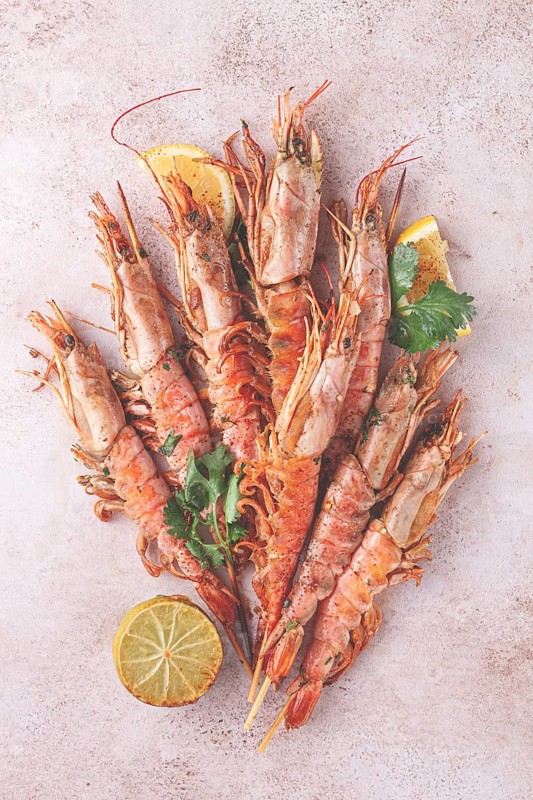 Shrimps on skewers, Grilled, spread on a marble surface, garnished, with lemon slices, and fresh herbs, view from above