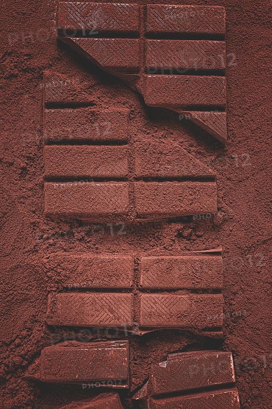 Chocolate bars broken and scattered on cocoa powder background with rich texture and color