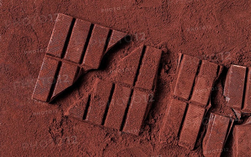Chocolate bars broken and scattered on cocoa powder background with rich texture and color