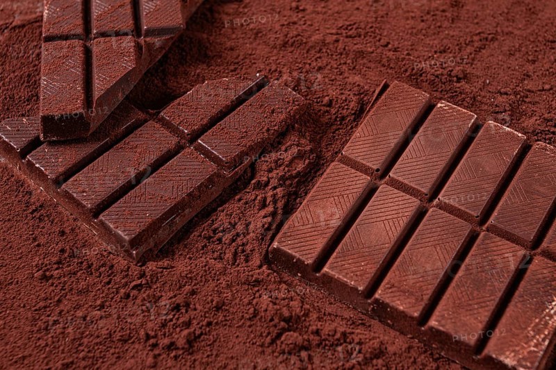 Chocolate bars broken and scattered on cocoa powder background with rich texture and color