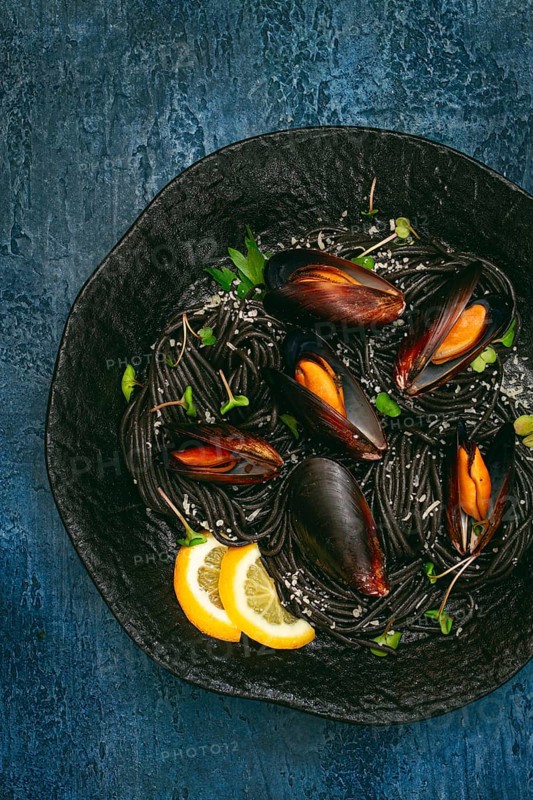 Spaghetti with black squid, black pasta, with boiled mussels, on a black plate, with parsley and parmesan cheese, close-up, selective focus, no people