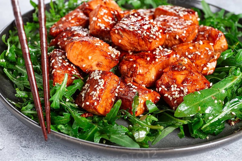 Fried salmon slices, teriyaki with sesame seeds, with arugula salad, top view