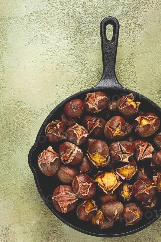 Roasted chestnuts, in an iron pan, wooden table, top view, no people, rustic style