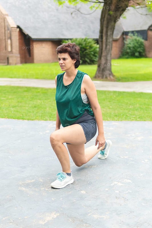 A focused woman performing a lunging stretch in a public park