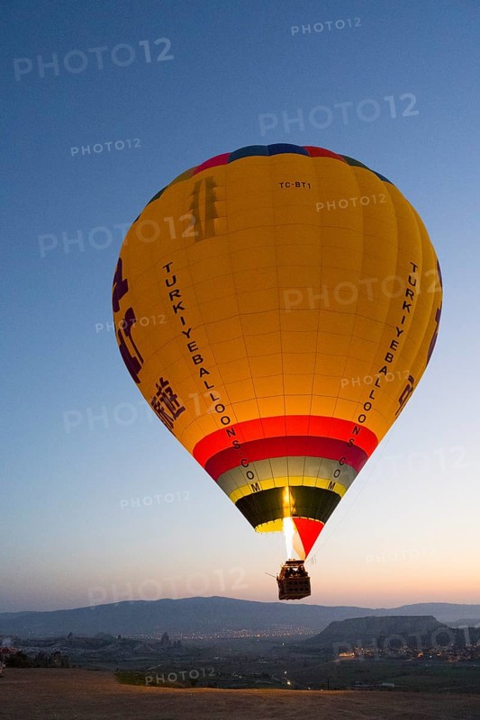 A large, luminous balloon floats over a clear mountainous landscape at dawn, Göreme National Park, Göreme Tarihî Millî Parki, Nevsehir Province, Nevsehir, Cappadocia, Cappadocia, Kapadokya, Cappadocia, Central Anatolia, Turkey