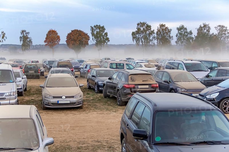 Dusty parking space scenery on a field including lots of dust covered cars at evening time in Southern Germany