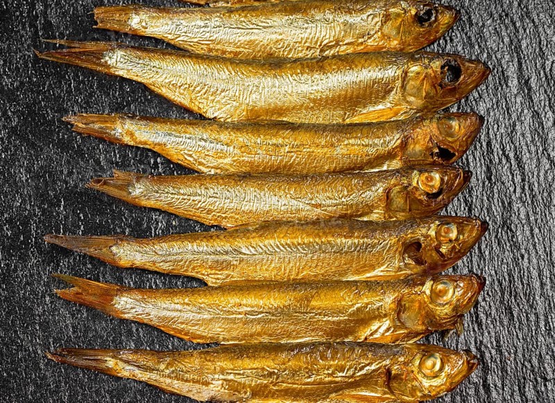 Arrangement with lots of fresh smoked sprats on dark stone slab