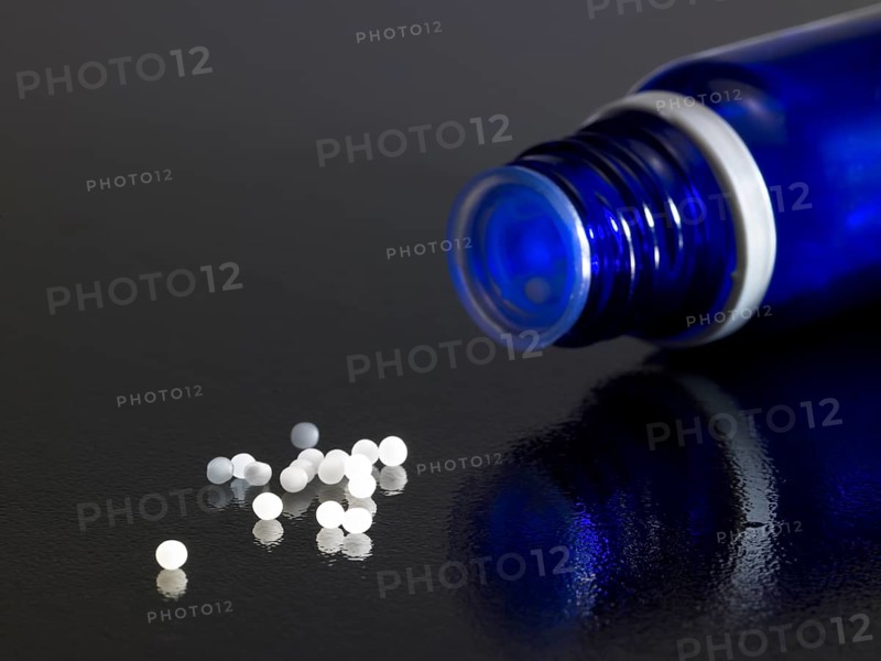 Detail of a open small blue bottle on dark reflective ground with globules around