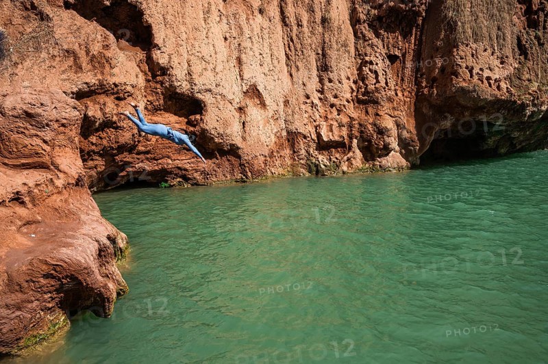 A Moroccan woman in swimsuit jumps headfirst into the water under a waterfall Ouzoud in Morocco