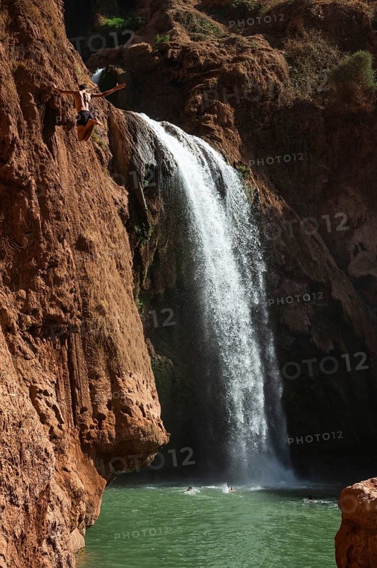 A Moroccan young man jumps from the high rock into the water under a waterfall Ouzoud