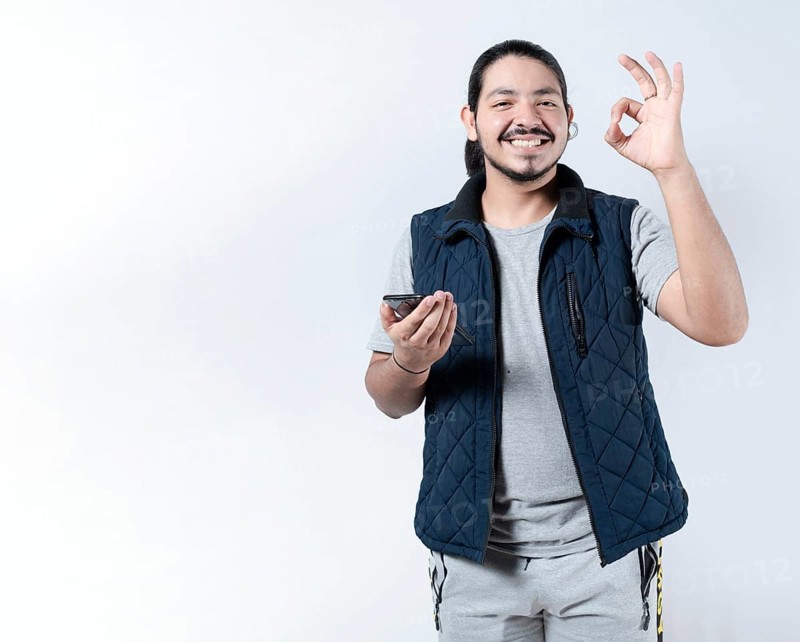 Smiling man gesturing approval with his phone in hand. Young man gesturing approval on the smartphone on isololated