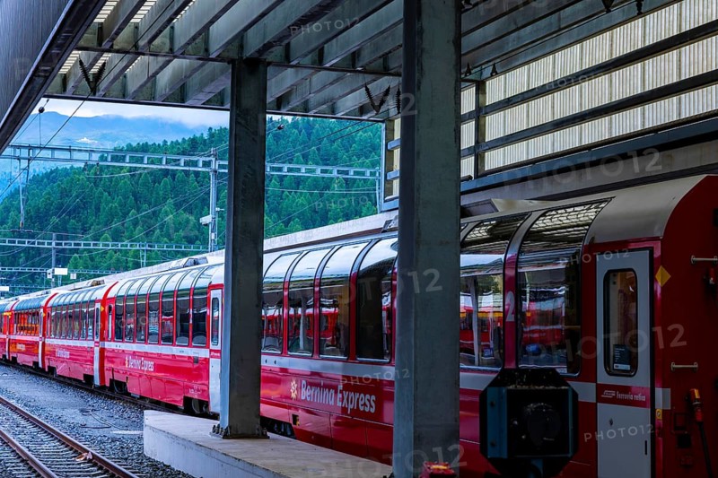 Railroad Station and Red Bernina Express Train with Mountain View in a Sunny Summer Day in Engadine, Maloja, St Moritz, Grisons, Switzerland