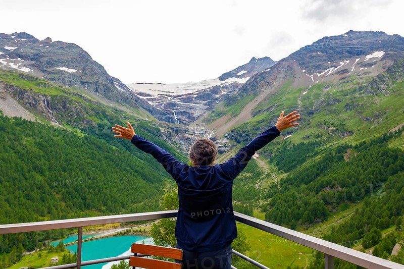 Woman with Arms Outstretched over the Beautiful Mountain Alp Grüm with Glacier and Alpine Lake Palü in the Swiss Alps in a Cloudy Summer Day in Poschiavo, Bernina, Grisons, Switzerland