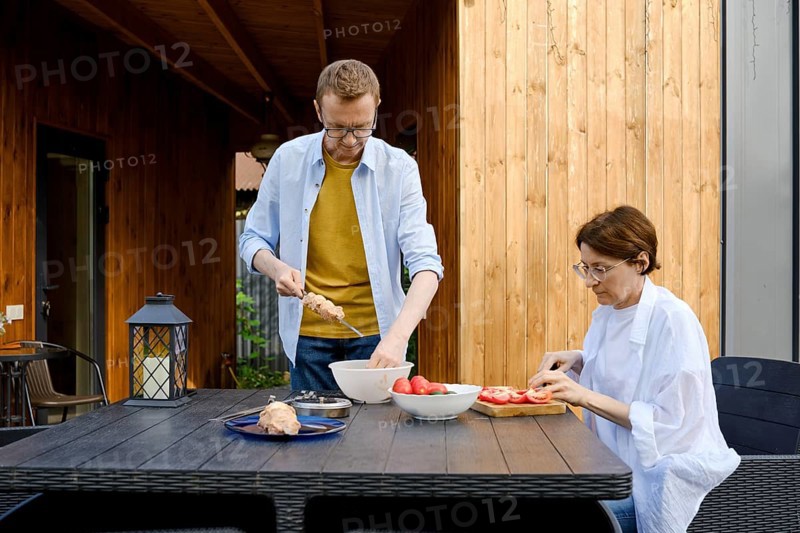 In a serene outdoor area, a man and woman are engaged in meal preparation at a wooden table