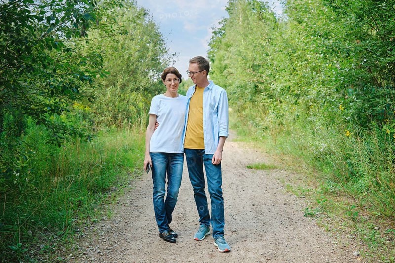 A middle-aged couple enjoys a stroll along a gravel path shaded by lush greenery. They smile at each other and have a leisurely conversation