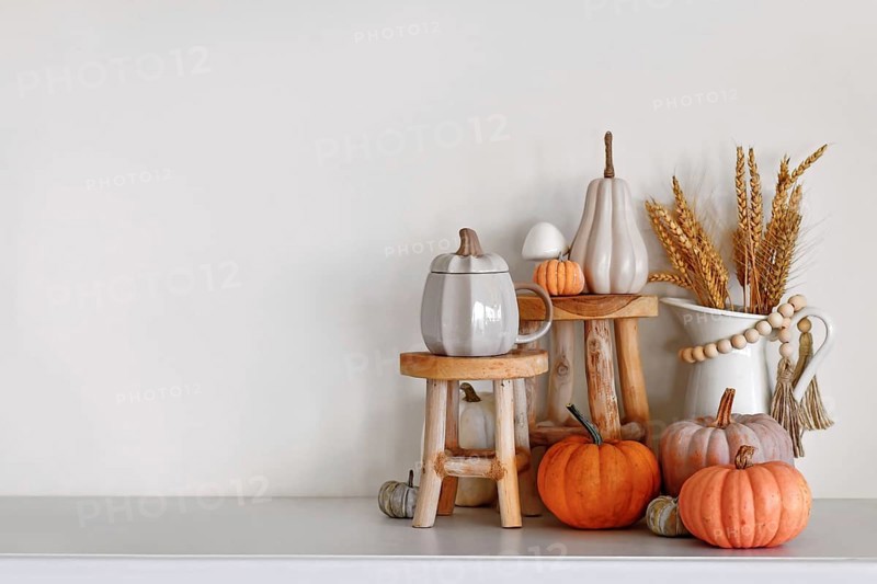 Seasonal fall home decor with wooden stands, pumpkins and vase with grains in front of white wall
