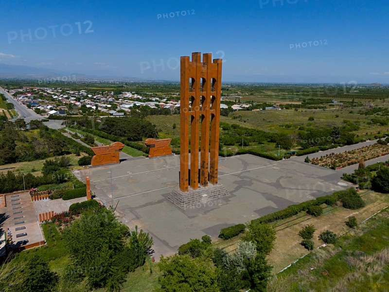 Large modern monument surrounded by landscape and small buildings under blue sky, aerial view, Sardarapat monument, Araks village, Armavir province, Armenia