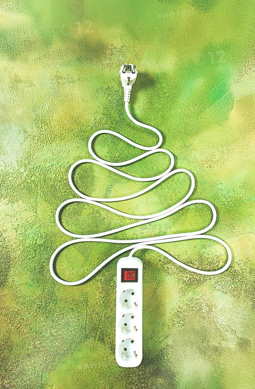 A power strip is arranged in the shape of a Christmas tree, artistically placed on a vibrant green and yellow backdrop. The design adds a playful touch to the festive atmosphere