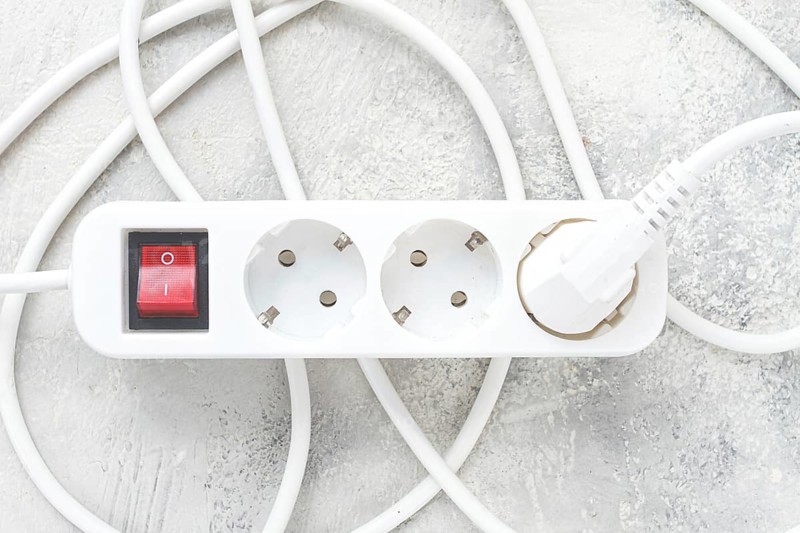 Power strip with multiple sockets and a switch in a cluttered setup on a textured surface during daytime